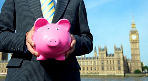 Businessman in suit holding a pink piggy back in front of the Houses of Parliament